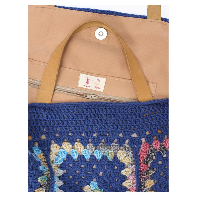 Puede incluir: Un bolso tote de crochet azul con un estampado floral colorido. El bolso tiene un asa de cuero marr&oacute;n claro y un interior marr&oacute;n claro. El bolso tiene un cierre de cremallera y un cierre de bot&oacute;n magn&eacute;tico. La etiqueta dentro del bolso dice "My Made".