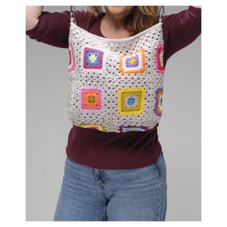 May include: A cream-coloured crocheted tote bag with colourful square patterns. The squares feature various colours like pink, yellow, blue, and orange. The bag has a shoulder strap and a simple, open design.