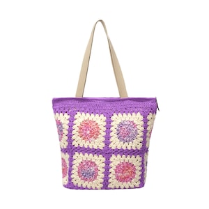 May include: A crocheted tote bag with a purple body and cream-colored handles. The bag features a floral pattern in shades of pink, purple, and cream. The bag has a zipper closure and is designed for carrying items.