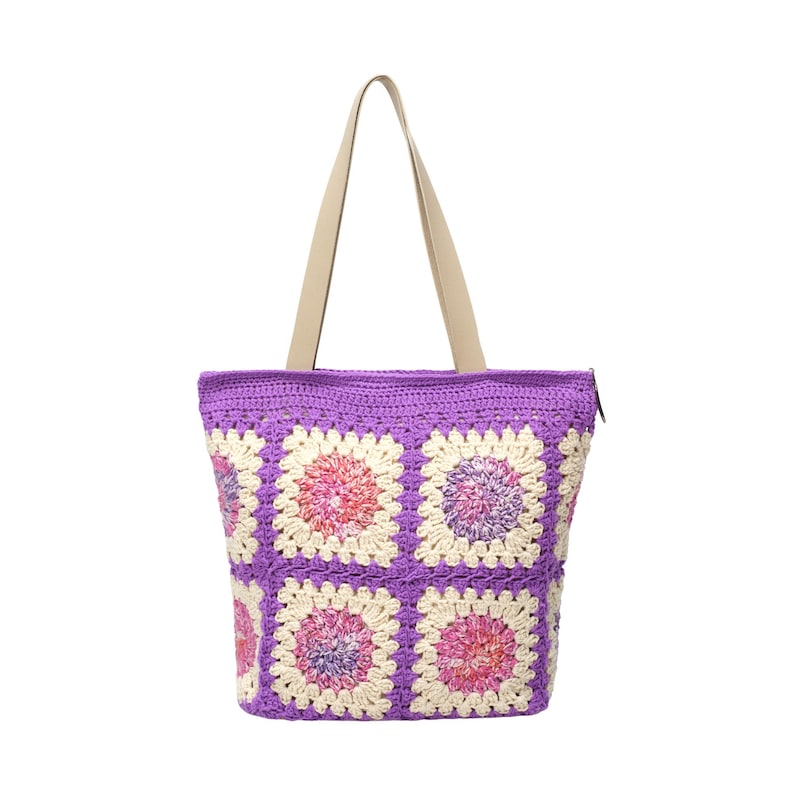 May include: A crocheted tote bag with a purple body and cream-colored handles. The bag features a floral pattern in shades of pink, purple, and cream. The bag has a zipper closure and is designed for carrying items.