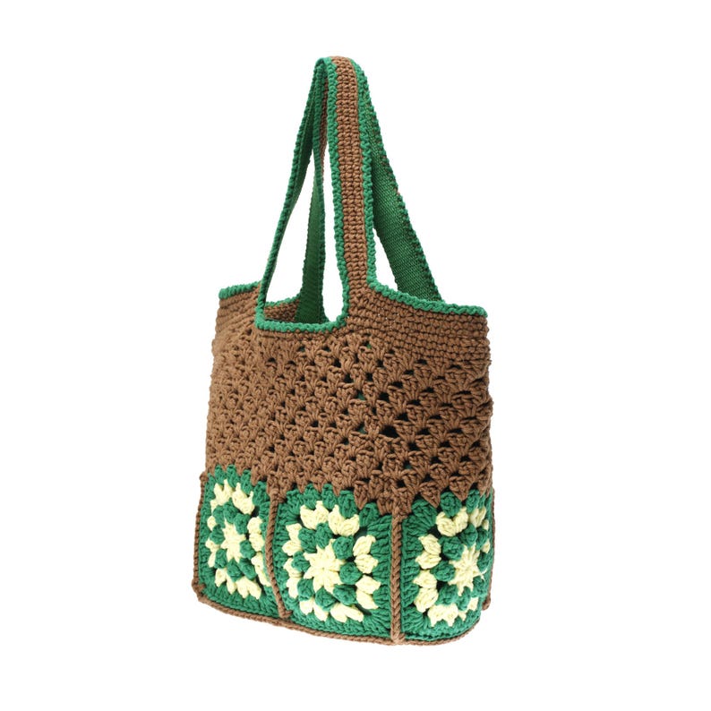 K&ouml;nnte beinhalten: Eine geh&auml;kelte Tragetasche in Braun und Gr&uuml;n. Die Tasche hat einen braunen K&ouml;rper mit gr&uuml;nen Verzierungen und Griffen. Der Boden der Tasche hat gr&uuml;ne und cremefarbene Blumenquadrate. Die Tasche ist aus weichem, strukturiertem Garn gefertigt.