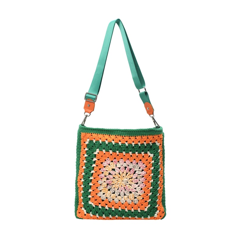 K&ouml;nnte beinhalten: Quadratische geh&auml;kelte Umh&auml;ngetasche mit farbenfrohem Granny-Square-Design. Die Tasche hat einen gr&uuml;nen Rand, eine orangefarbene und cremefarbene Mitte sowie einen t&uuml;rkisfarbenen Riemen mit Lederakzenten. Ein einzigartiges, handgefertigtes Accessoire.