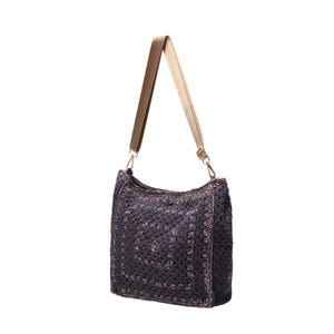 May include: A dark purple crochet shoulder bag featuring a square pattern design. The bag includes a wide, adjustable beige nylon strap attached with gold-toned metal swivel clasps on each side, providing a functional and textured accessory.