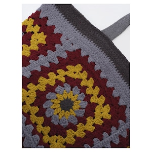May include: A crochet tote bag featuring a square granny motif pattern in shades of mustard yellow, deep burgundy, and light gray. The bag is constructed with a dark gray solid crochet border and includes a matching dark gray fabric strap.