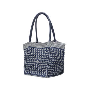 May include: A handmade tote bag with a blue and grey crochet pattern. The bag features a geometric design and has dark blue leather handles. The top edge and handles are a darker shade of blue.