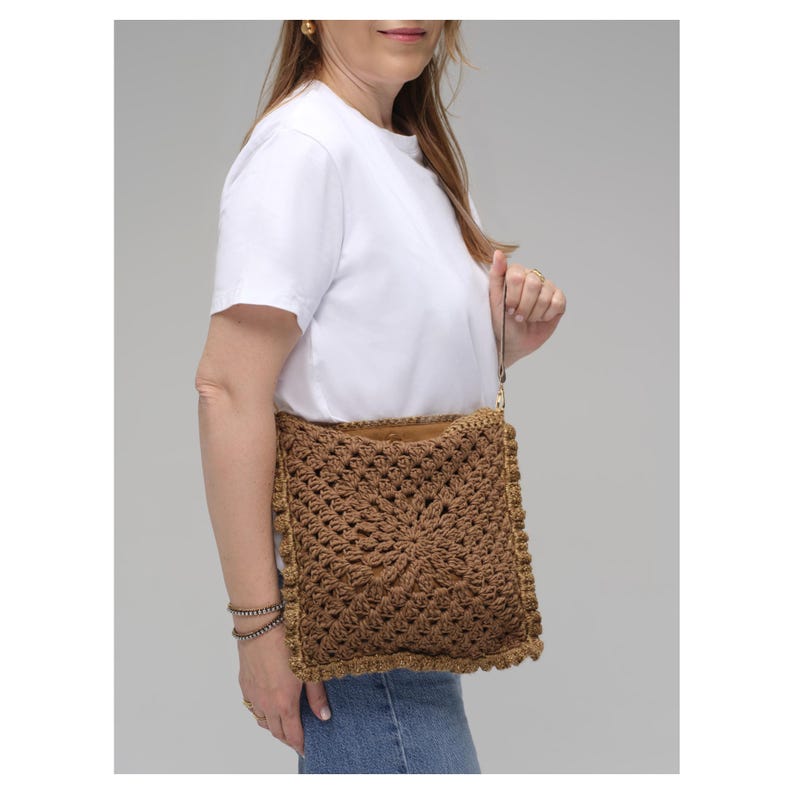 May include: A square brown crochet handbag featuring a textured granny square pattern with a central star motif. The bag has a thin wrist strap, a visible tan interior lining, and a decorative border edge, providing a compact accessory option.