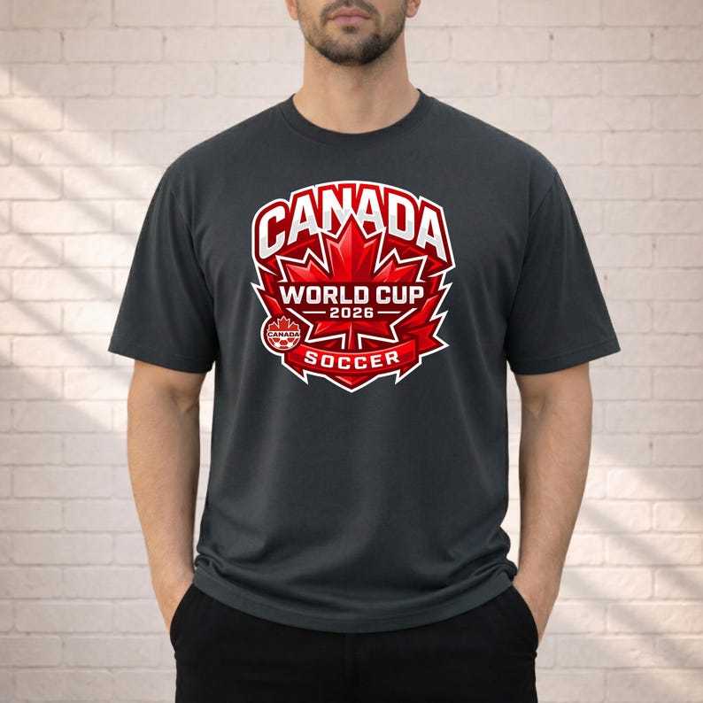 May include: Dark gray t-shirt featuring a red and white graphic for the Canada World Cup 2026 Soccer. The design includes a maple leaf and the text "CANADA WORLD CUP 2026 SOCCER".