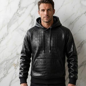 Peut inclure: Un sweat à capuche noir à manches longues présentant un motif texturé en peau de crocodile sur tout le vêtement. Le sweat comprend une capuche assortie avec des cordons noirs, une poche kangourou avant, ainsi que des poignets et un ourlet côtelés.