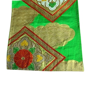 May include: A bright green fabric panel featuring embroidered diamond-shaped motifs with red, yellow, and silver floral patterns. The textile includes gold-colored cloud-like shapes with a woven texture and red geometric borders throughout the design.