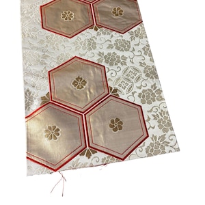 May include: A rectangular fabric panel featuring a white background with a tonal floral pattern. The surface is decorated with five large, gold-coloured hexagonal shapes, each outlined in red thread and centred with a small gold flower motif.