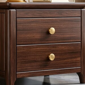 May include: A dark brown wooden nightstand featuring two stacked drawers with a visible wood grain pattern. Each drawer is equipped with a single, round, brushed gold-toned metal knob centered on the front panel of the drawer face.