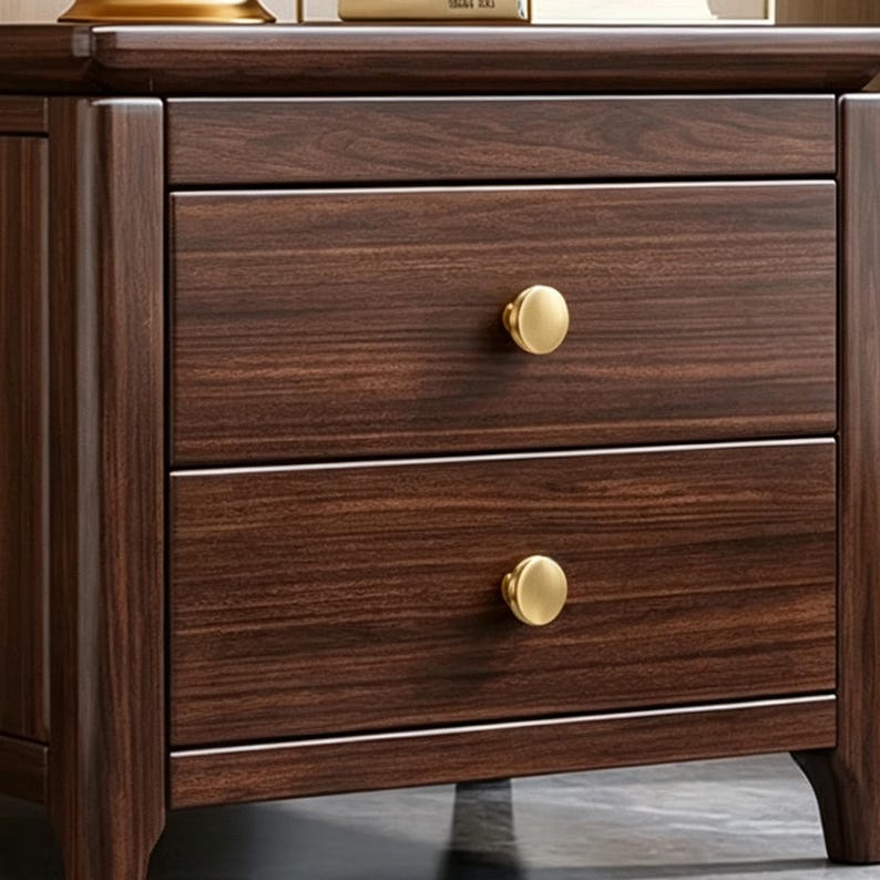 May include: A dark brown wooden nightstand featuring two stacked drawers with a visible wood grain pattern. Each drawer is equipped with a single, round, brushed gold-toned metal knob centered on the front panel of the drawer face.