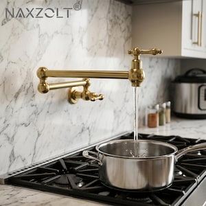 May include: A gold-toned, wall-mounted pot filler faucet with a swing arm design. Water flows from the faucet into a stainless steel pot on a gas stovetop. The faucet is mounted on a marble backsplash. The brand name "NAXZOLT" is visible.