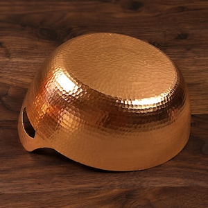 May include: A round, hammered copper bowl with a metallic, reddish-brown finish. The exterior surface features a dense, textured pattern of small, concave indentations. A single, small, semi-circular cutout is visible on the lower side rim.