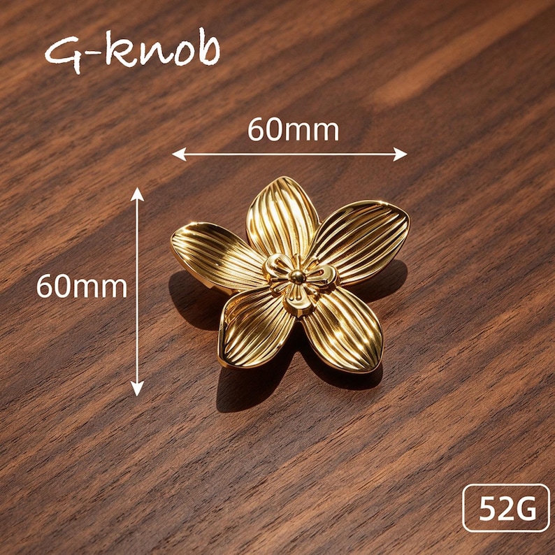 May include: A gold-colored flower-shaped knob labeled G-knob, featuring five petals with vertical ridges and a central detail. The knob measures 60mm by 60mm and weighs 52g, as indicated by the text and arrows visible in the image.