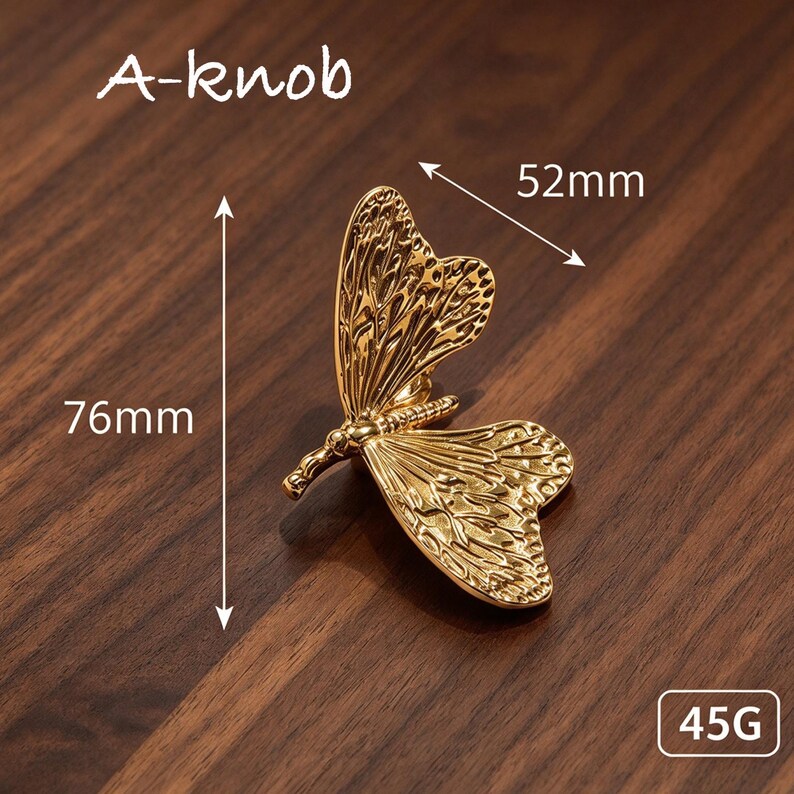 May include: A gold-colored butterfly-shaped knob labeled A-knob. The design features intricate wing textures. Dimensions are indicated as 76mm in height and 52mm in width, with a weight of 45g. The object is a metallic hardware piece.