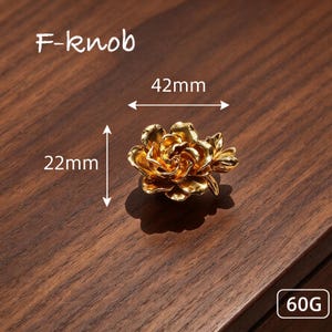 May include: A gold-colored metal cabinet knob shaped like a blooming rose. The knob features the text F-knob, a width of 42mm, a height of 22mm, and a weight of 60G. The metallic surface reflects light, creating highlights and shadows on the petals.