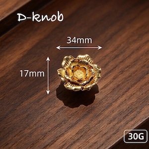 May include: A gold-colored flower-shaped D-knob with a textured center and layered petals. The knob measures 34mm in width and 17mm in height, with a weight of 30G. The design features a metallic finish with detailed petal contours.