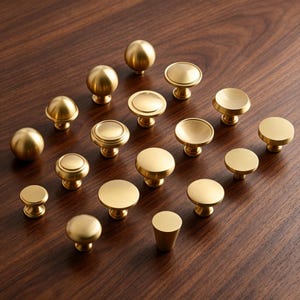 May include: A collection of various brass-colored metal cabinet knobs in different shapes, including spherical, flat-topped, and tapered designs. Each knob features a smooth, matte finish and a circular base, arranged in a grid-like formation.