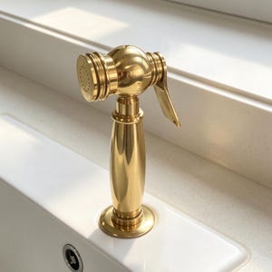 Peut inclure: Un pulvérisateur latéral pour évier de cuisine en finition dorée polie, doté d'un corps cylindrique, d'une tête arrondie avec un motif de pulvérisation circulaire et d'un levier latéral. L'accessoire présente une finition métallique lisse.