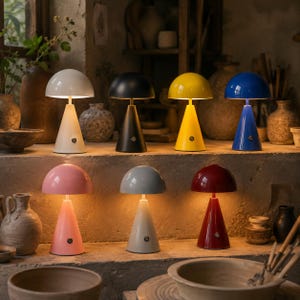 May include: Seven mushroom-shaped table lamps with conical bases and rounded shades, each featuring a small circular power button on the front. The lamps are displayed in white, black, yellow, blue, pink, gray, and red, emitting a warm light.