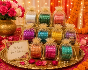 May include: A collection of twelve sets of metallic bangles, each housed in a sheer gold drawstring pouch. The bangles come in silver, green, red, purple, blue, yellow, and orange. A rectangular card reads Mehendi Love & Blessings.