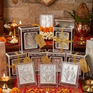 May include: A collection of silver-toned rectangular plaques featuring a relief of two figures, each displayed in a clear acrylic stand. Several plaques are packaged in brown and white boxes labelled 1 NO. STAND with gold ribbon bows and tags.