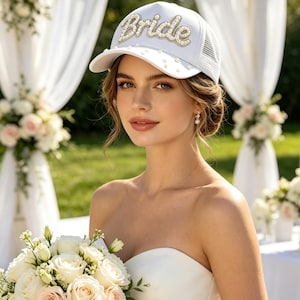 May include: A white baseball cap featuring the word Bride in pearl-embellished lettering across the front. The cap includes a mesh back panel and is decorated with small, scattered white pearls on the brim and front crown area.