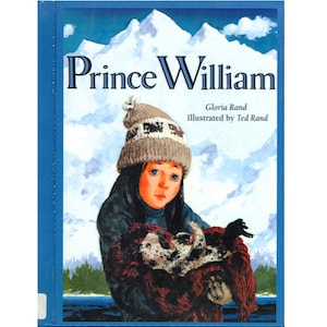 May include: A book cover titled "Prince William" by Gloria Rand, illustrated by Ted Rand. The cover features a young person wearing a knit hat and holding a seal pup. The background shows snow-capped mountains and a blue sky.