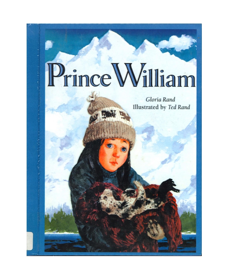 May include: A book cover titled "Prince William" by Gloria Rand, illustrated by Ted Rand. The cover features a young person wearing a knit hat and holding a seal pup. The background shows snow-capped mountains and a blue sky.