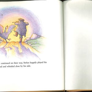 May include: A vibrant illustration from a children's book shows a man playing a flute, with a goose nearby. The scene is set on a hill with a fence, under a soft, glowing sky. Text at the bottom describes the scene.