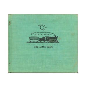 May include: A rectangular book with a light green textured cover. Centered on the front is a black line drawing of a steam train on tracks with a sun above it. Below the train, the text "The Little Train" is printed in black, serif font.
