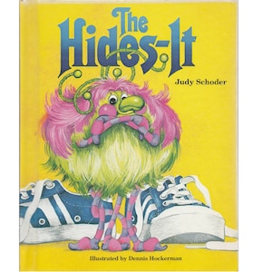 May include: A yellow book cover with the title "The Hides-It" in blue letters. A green and pink furry creature with a purple and pink striped body is standing on a blue and white sneaker. The book is illustrated by Dennis Hockerman and written by Judy Schoder.