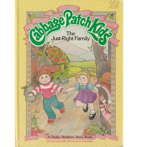 May include: A book cover featuring two Cabbage Patch Kids dolls, a girl with red hair and a girl with blonde hair, walking through a forest. The book title is "Cabbage Patch Kids The Just-Right Family" and the subtitle is "A Parker Brothers Story Book".