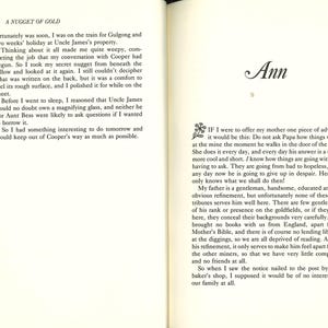 May include: Open book with text on both pages. The left page has the title "A NUGGET OF GOLD" and text. The right page has the name "Ann" in cursive and more text. The book is open to a chapter.
