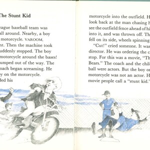 May include: An open book page with text and illustrations. The title "The Stunt Kid" is at the top. An illustration shows a boy on a motorcycle. The text describes a baseball team and a movie scene.