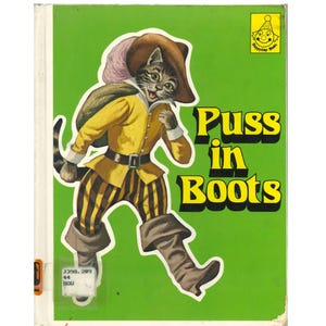 May include: A vintage children's book cover featuring a cartoon cat in a yellow jacket, brown striped pants, and boots. The title "Puss in Boots" is in large yellow letters on a green background. A small logo is in the upper right corner.
