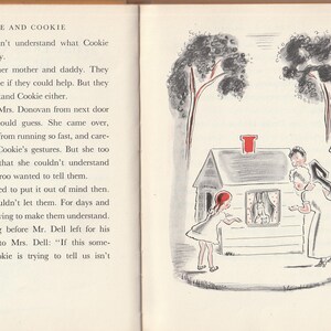 May include: A black and white illustration of a small house with a red chimney. Four people are standing outside the house, looking at a kangaroo inside the window. The text "EVIE AND COOKIE" is at the top of the page.