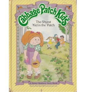 May include: A book cover featuring a cartoon illustration of a Cabbage Patch Kid doll with red hair and a purple dress. The title of the book is "The Shyest 'Kid in the 'Patch" and it is a Parker Brothers Story Book.