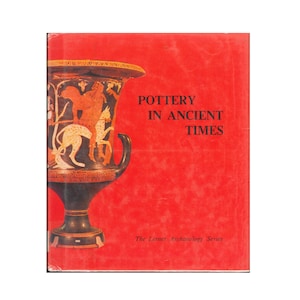 May include: A hardcover book titled Pottery in Ancient Times from The Lerner Archaeology Series. The bright red cover features a large illustration of a black and orange ancient Greek vase decorated with a figure riding a spotted animal.