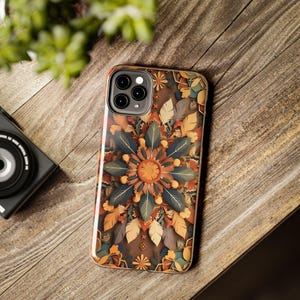 Pode incluir: Uma capa de smartphone com um padrão simétrico inspirado em mandalas, com formas de folhas e penas em camadas em tons de laranja queimado, azul-petróleo profundo, amarelo mostarda e creme, centrado num núcleo circular laranja texturizado.