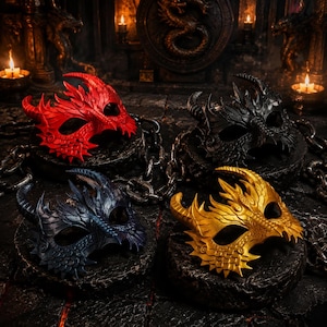 May include: Four dragon-themed masquerade masks in red, black, blue, and gold. Each mask features intricate details, horns, and a textured surface. The masks are displayed on dark, textured pedestals, with chains and candles in the background.