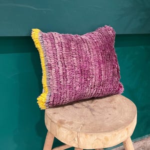 May include: A square throw pillow featuring a shaggy, textured pile in shades of magenta and purple. The left edge of the pillow is accented with a vertical strip of bright yellow fringe, providing a distinct color contrast to the main body.