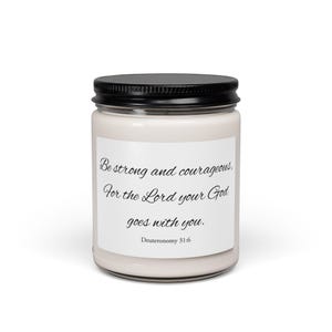 Peut inclure: Une bougie en pot de verre transparent avec un couvercle en métal noir, remplie de cire blanc cassé. Une étiquette rectangulaire blanche porte le texte imprimé en noir : Be strong and courageous, For the Lord your God goes with you. Deuteronomy 31:6.