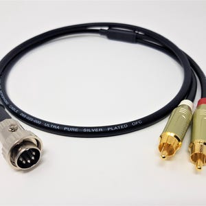 May include: A black microphone cable with silver connectors and gold-coloured RCA connectors. The cable has the text "ULTRA PURE SILVER PLATED OFC" printed on it. The cable is designed for audio equipment.