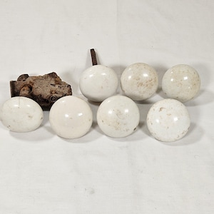 May include: A collection of antique door hardware, including seven white ceramic doorknobs and a rusty metal latch. The doorknobs are spherical and show signs of age, with slight discoloration. The latch is rectangular and heavily weathered.