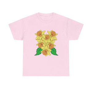 May include: A pale pink t-shirt with a floral design. The design features yellow daffodils with orange centres and green leaves. The daffodils are arranged vertically, creating a bright and attractive floral pattern.
