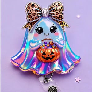May include: An iridescent ghost badge reel featuring a large leopard print bow at the top. The ghost has large black eyes, pink cheeks, and a small smile, holding an orange jack-o'-lantern bucket filled with colourful candies and treats.