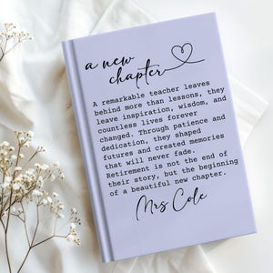 May include: A light purple hardcover book featuring the text 'a new chapter' with a heart icon, followed by a paragraph honoring a teacher's retirement and the name 'Mrs Cole' printed in black ink on the front cover of the book.