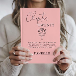 May include: A pink hardcover book with black text that reads Chapter TWENTY, followed by a line drawing of three roses. Below the flowers, the text reads: BEHIND YOU, ALL YOUR MEMORIES, BEFORE YOU, ALL YOUR DREAMS, AROUND YOU, ALL WHO LOVE YOU, WITHIN YOU, ALL YOU NEED. DANIELLE.